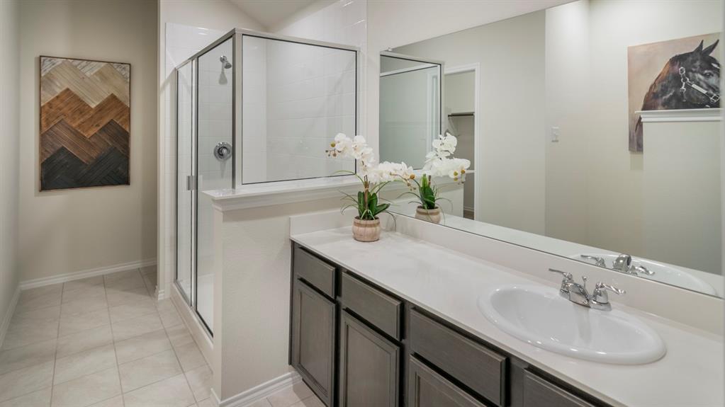 Bathroom featuring a spacious vanity with an undermount sink, a full-width mirror, a glass-enclosed shower, and light-colored tile flooring