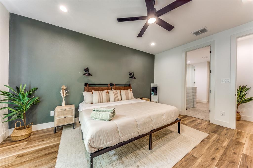 Bedroom featuring a dark accent wall, wood-finish flooring, a contemporary ceiling fan with integrated lighting, recessed lighting, and a doorway to a bathroom with tiled walls