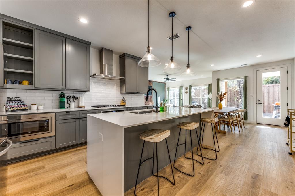 Open-concept kitchen featuring an oversized island with seating, pendant lighting, stainless steel appliances, and wood-finish flooring