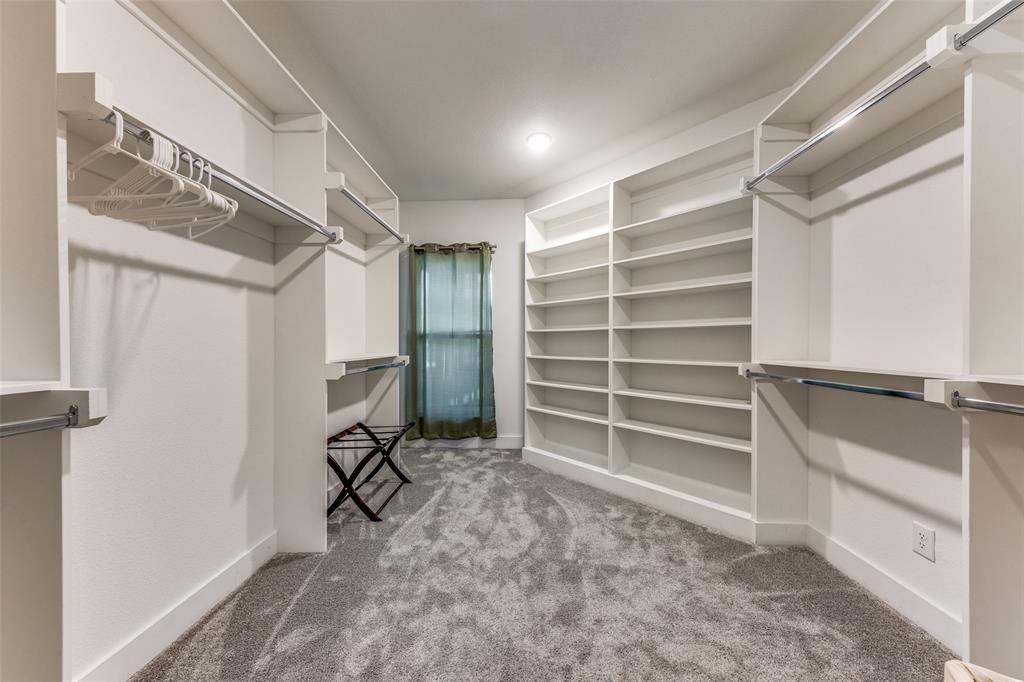 Spacious custom closet featuring extensive built-in shelving, multiple hanging rods, and plush gray carpeting