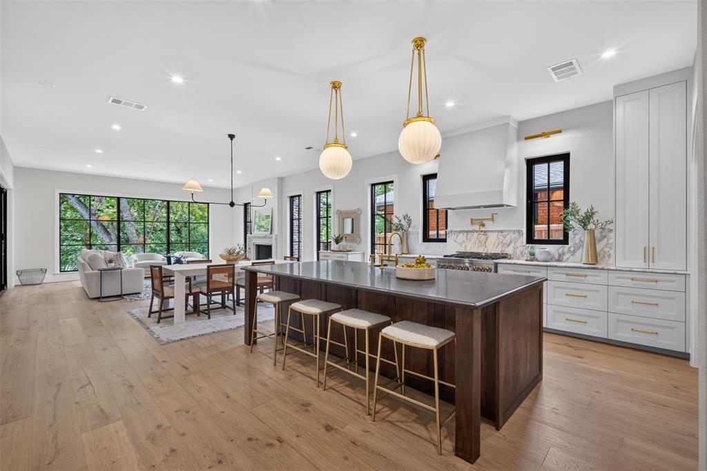 Gourmet kitchen featuring a large central island, white cabinetry, integrated range hood, and light wood-finish flooring