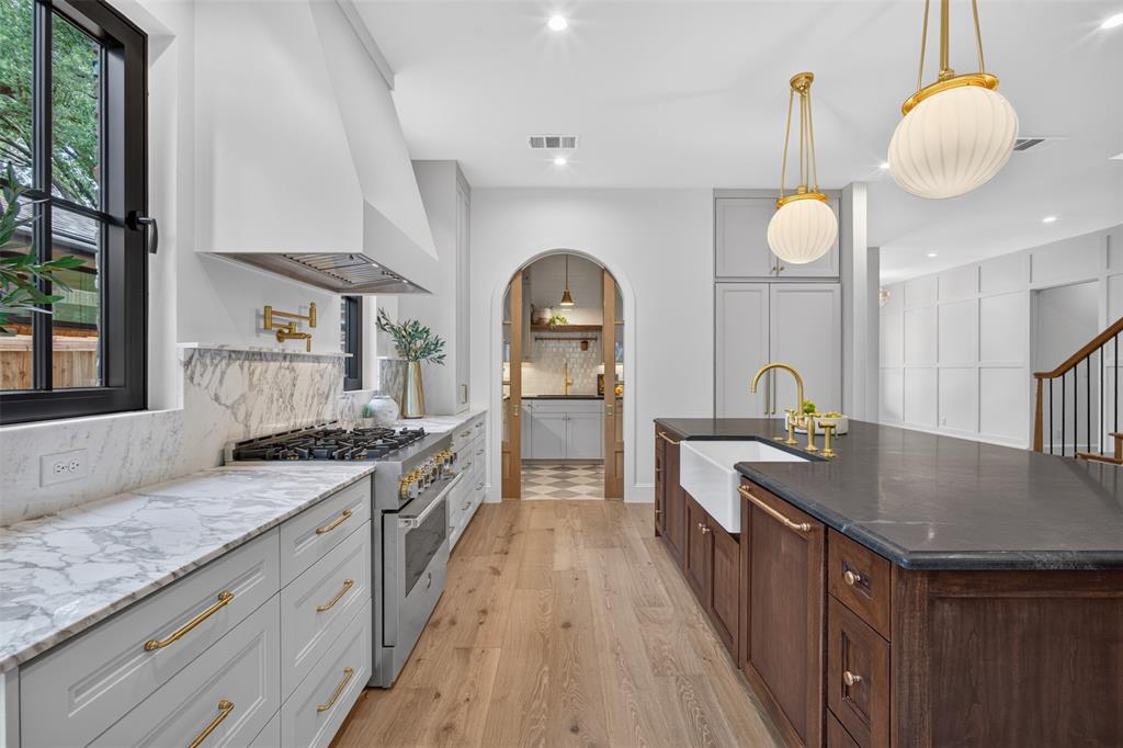Gourmet kitchen featuring a large central island with a farmhouse sink, stainless steel range, light wood-finish flooring, marble-finish countertops and backsplash, and a custom range hood