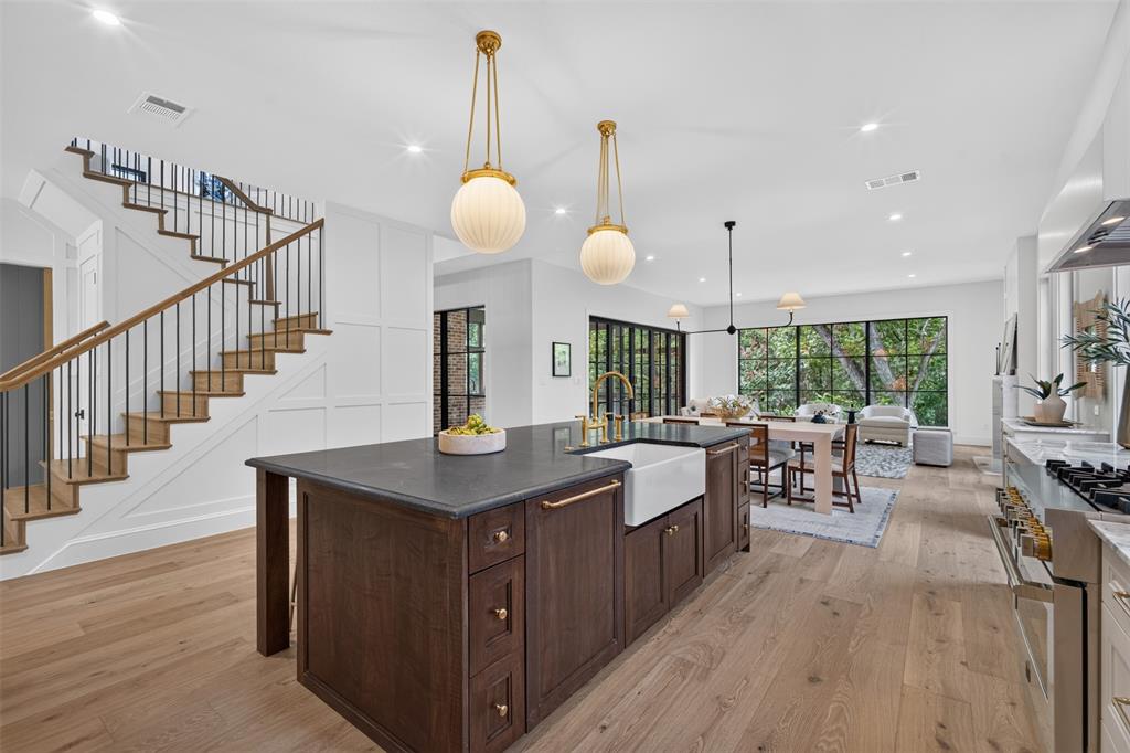 Open-concept living space featuring a dark wood kitchen island with an integrated farmhouse sink, light wood-finish flooring, and a contemporary staircase with dark iron balusters