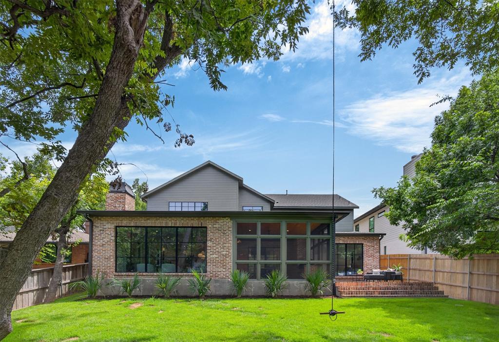 Expansive rear lawn featuring a brick exterior with large windows, a screened porch, a multi-tiered brick patio, and mature trees providing natural shading