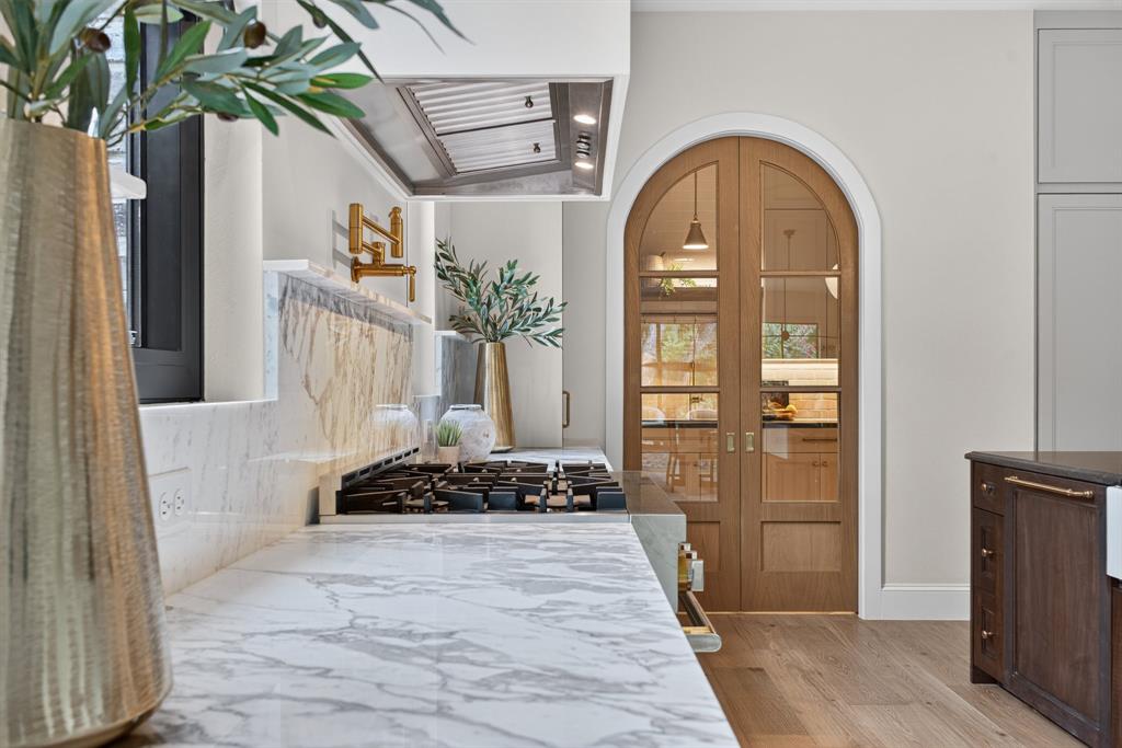 Gourmet kitchen featuring a built-in gas range, marble countertops and backsplash, a stainless steel range hood, and a gold-tone wall-mounted pot filler