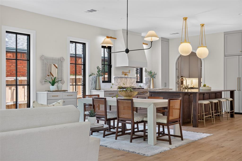 Open-concept living space featuring wood-finish flooring, a kitchen island with seating, a built-in range hood, and multiple windows with black framing