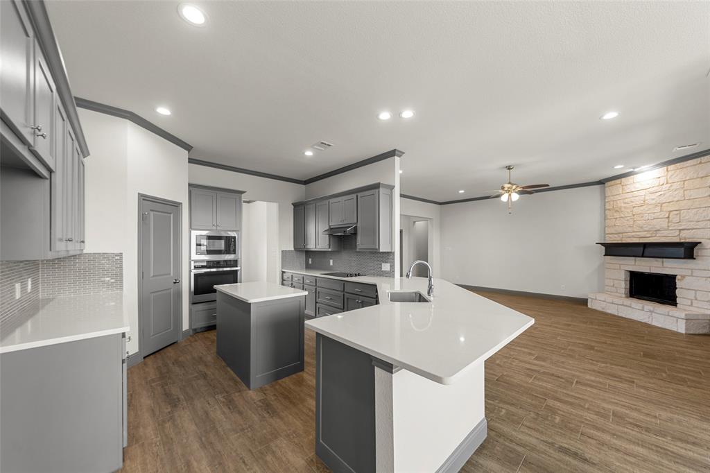Open-concept kitchen and living area featuring wood-finish flooring, recessed lighting, and a stone-clad fireplace with a dark wood mantle