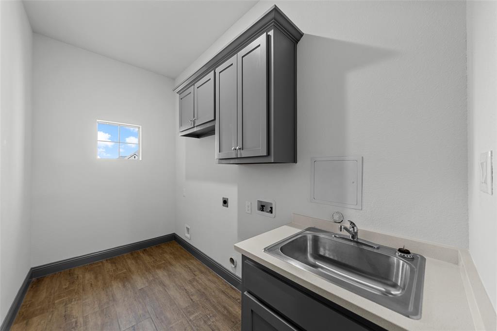Utility room featuring wood-finish flooring, a wall-mounted window, and built-in cabinetry with a countertop and stainless steel sink