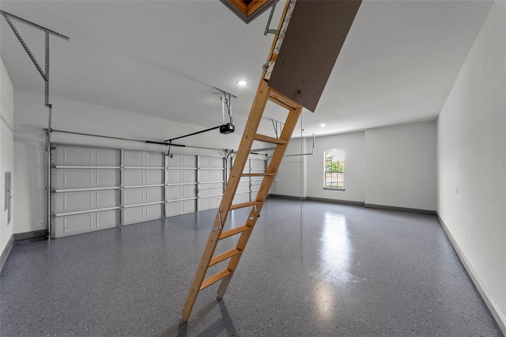 Spacious garage featuring a durable epoxy-coated floor, automatic garage door opener, attic access ladder, recessed lighting, and an arched window