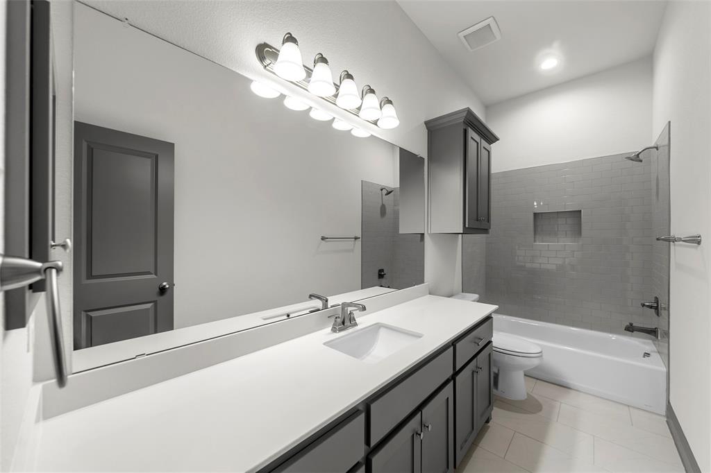 Bathroom featuring a large vanity mirror, an undermount sink, ample counter space, dark wood-finish cabinetry, and a subway tile shower surround with an integrated niche