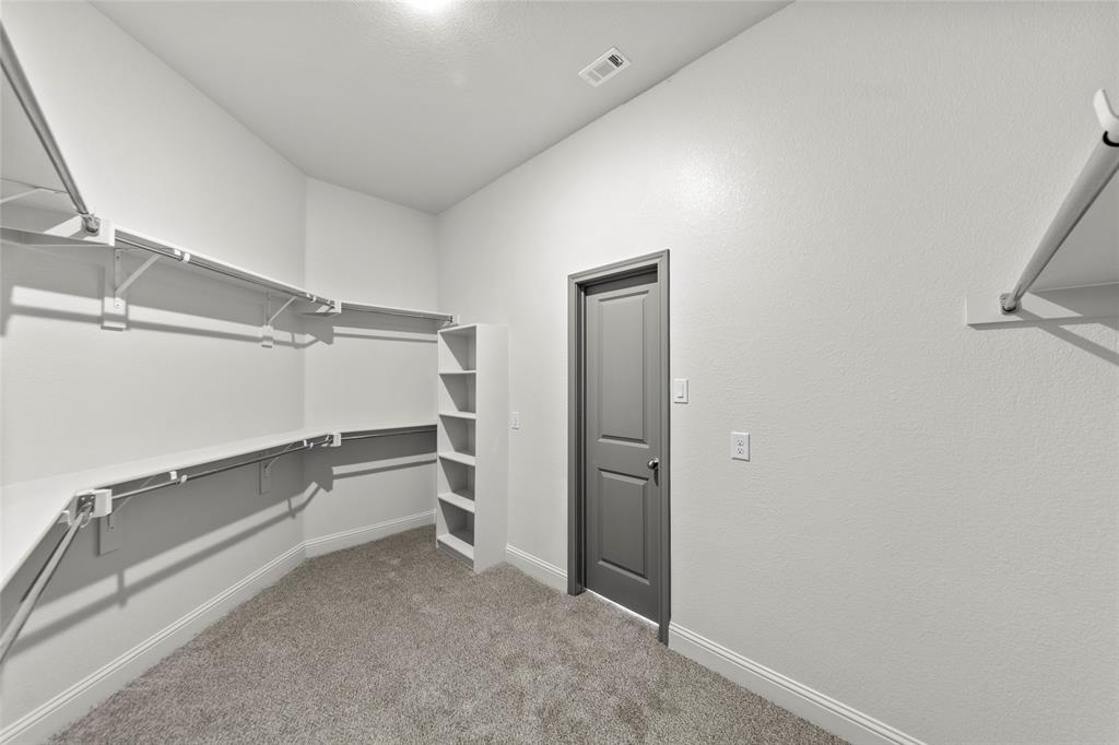 Walk-in closet featuring built-in shelving, hanging rods, an integrated storage tower, light gray carpeting, and white baseboards