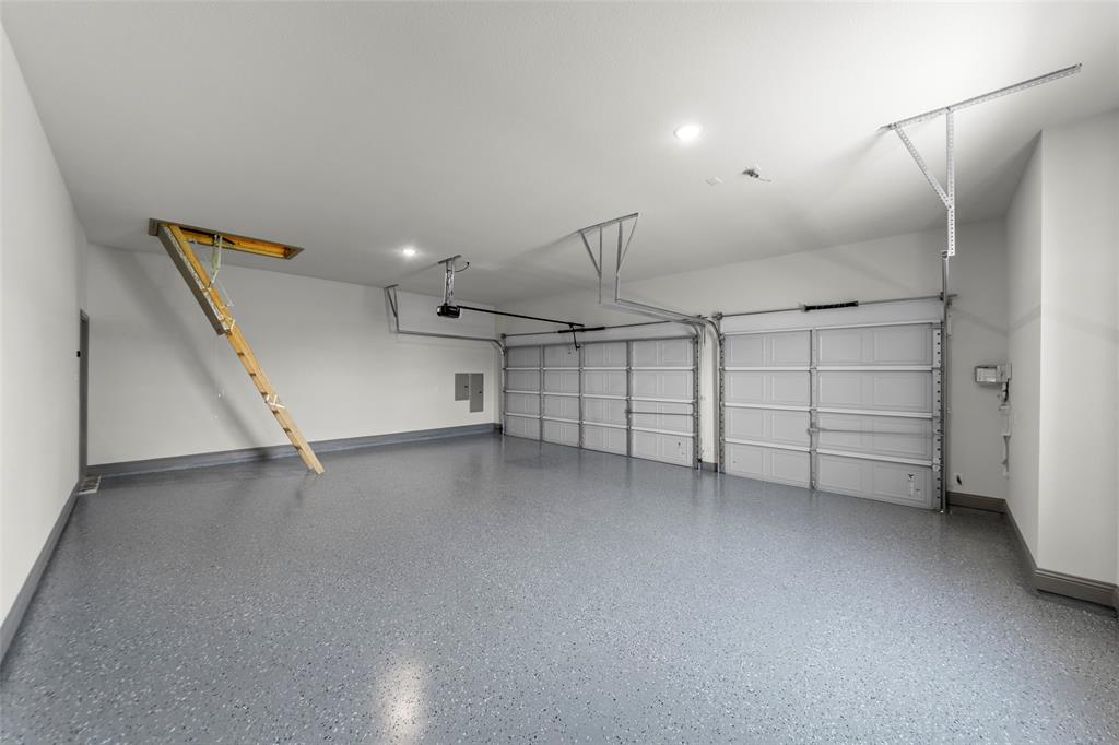 Two-car garage featuring a speckled epoxy floor coating, white walls, and a pull-down attic access ladder