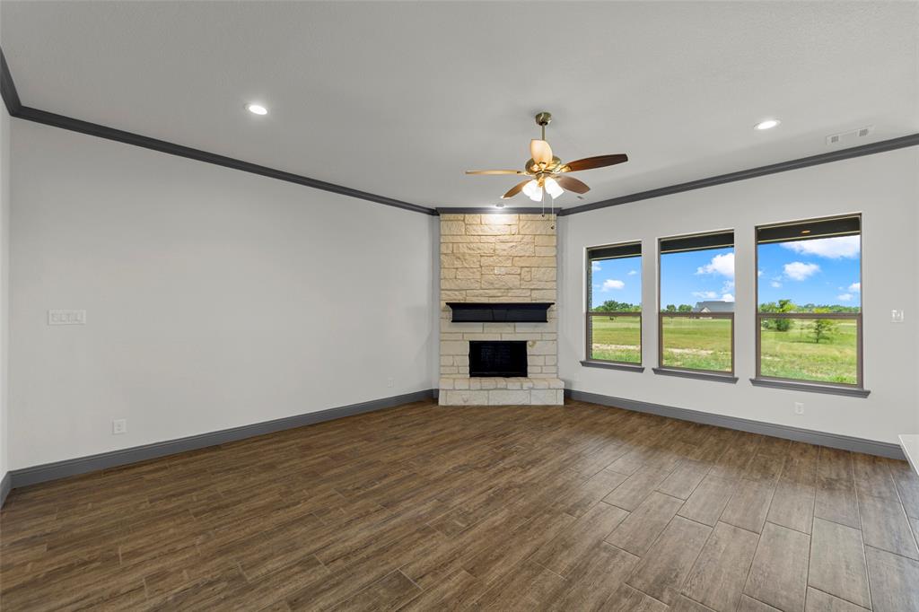 Living area featuring wood-finish flooring, a stone-clad fireplace with a dark mantel, three large windows, a ceiling fan with integrated lighting, and recessed ceiling lights