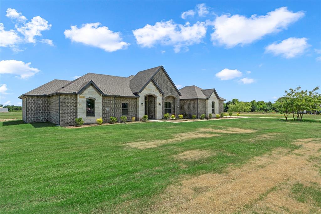 Brick and stone exterior featuring an arched entryway, gabled rooflines, and a spacious front lawn
