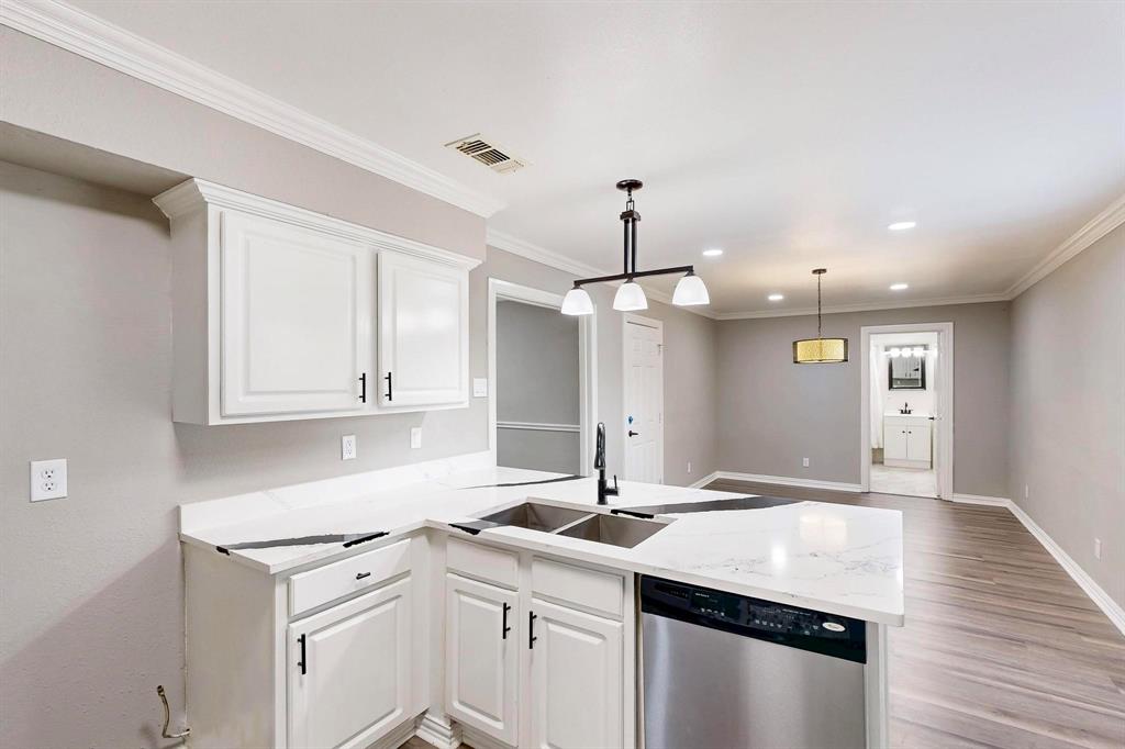 Kitchen featuring stainless steel dishwasher, a sink, a peninsula, baseboards, and white cabinets