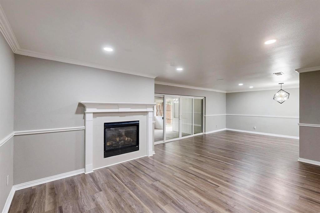 Unfurnished living room featuring wood finished floors, a glass covered fireplace, ornamental molding, baseboards, and recessed lighting