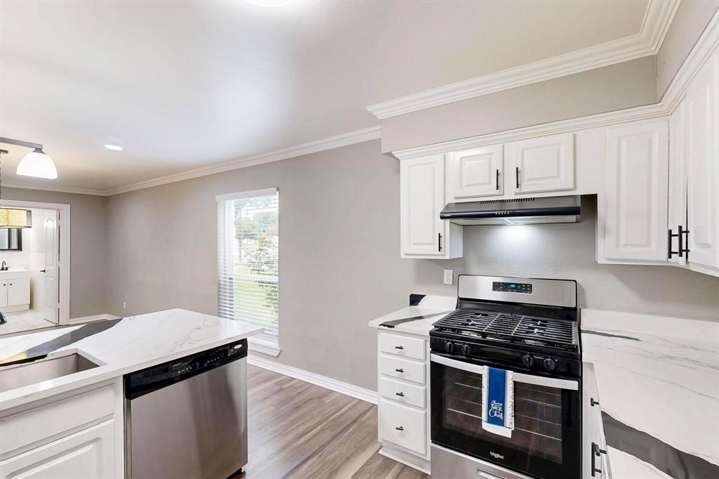 Kitchen featuring stainless steel appliances, under cabinet range hood, white cabinetry, crown molding, and light wood finished floors