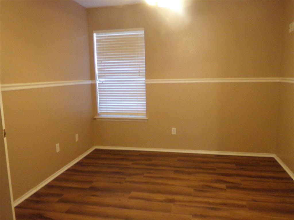 Room featuring wood-finish flooring, a window with blinds, and neutral-toned walls with decorative trim