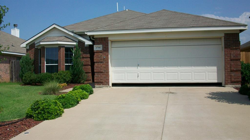 Brick facade residence featuring a two-car garage, concrete driveway, bay window, and established front landscaping