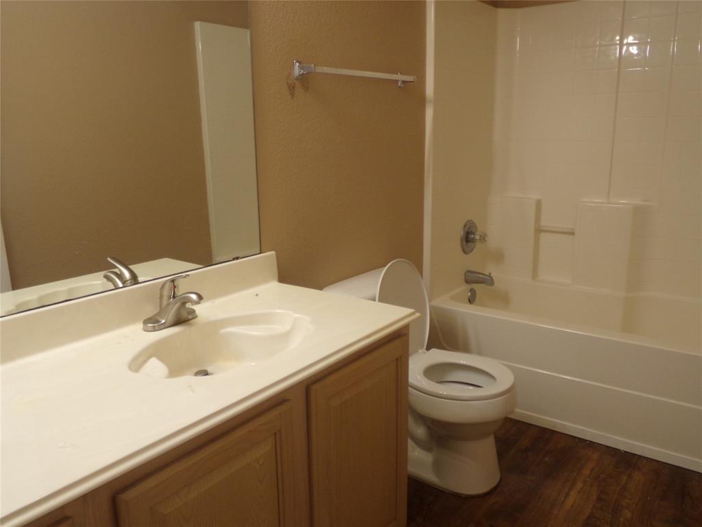 Hall Bathroom featuring wood-finish flooring, a vanity with a light-colored countertop and integrated sink, chrome-finish faucet, and a shower-tub combination with a white surround