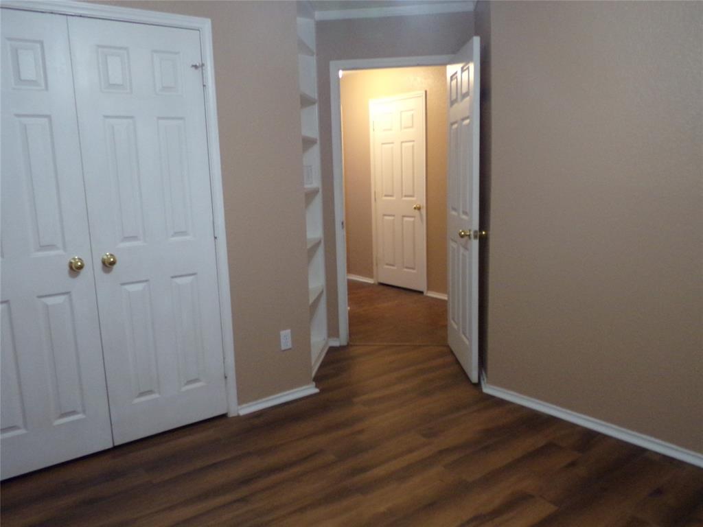 Wood-finish flooring throughout, featuring a double-door closet with gold-toned hardware, white baseboards, and built-in shelving