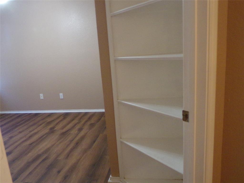 Built-in shelving unit with multiple white shelves, set against a neutral painted wall and wood-finish flooring