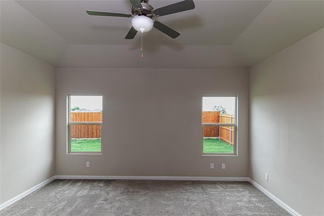Spacious room featuring a tray ceiling with a ceiling fan and light fixture, two windows, gray carpeting, and white baseboards