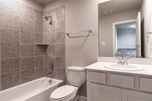 Bathroom featuring a white bathtub, gray tiled shower surround with built-in shelf, white vanity with an integrated sink, and brushed nickel fixtures