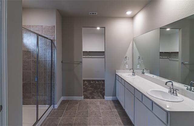 Bathroom featuring a dual vanity with white cabinetry and integrated sinks, a large wall-mounted mirror, recessed lighting, and a walk-in shower with tile surround and glass enclosure