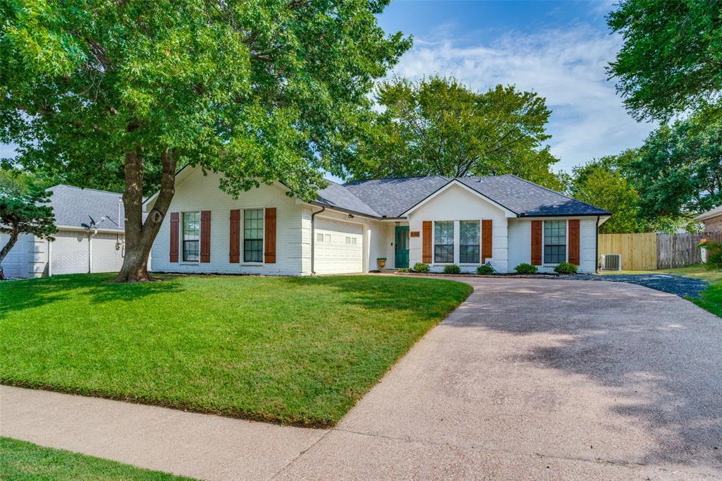White exterior featuring a dark asphalt shingle roof, brown decorative shutters, a light-colored concrete driveway, and a manicured lawn