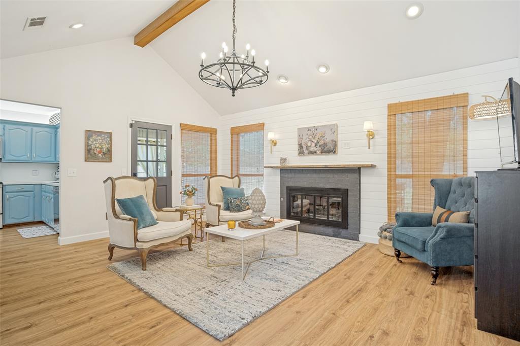Vaulted ceiling with exposed wood beam, wood-finish flooring, and a modern fireplace with a dark surround and wood mantel