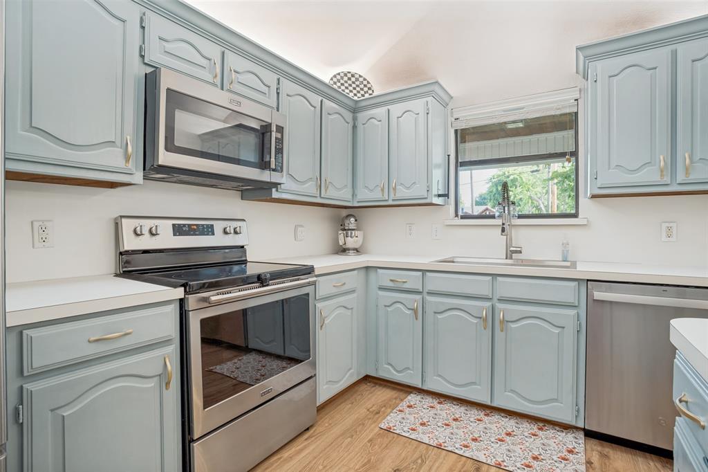 Kitchen featuring light blue cabinetry with gold-toned hardware, white countertops, and wood-finish flooring