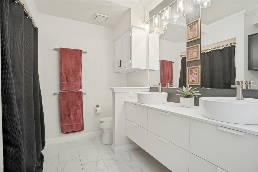 Spacious bath featuring dual vessel sinks, white cabinetry, a large mirror, chrome fixtures, and tile flooring