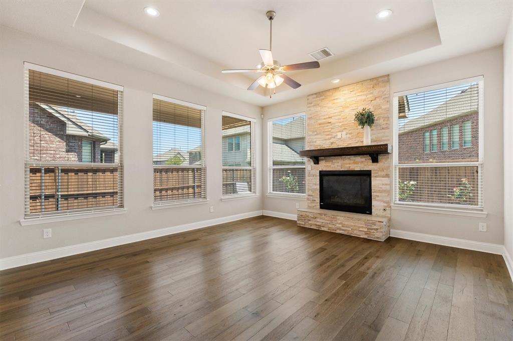 Stone-clad fireplace with a dark wood-finish mantel, wood-finish flooring, and a ceiling fan Stone-clad fireplace with a dark wood-finish mantel, wood-finish flooring, and a ceiling fan