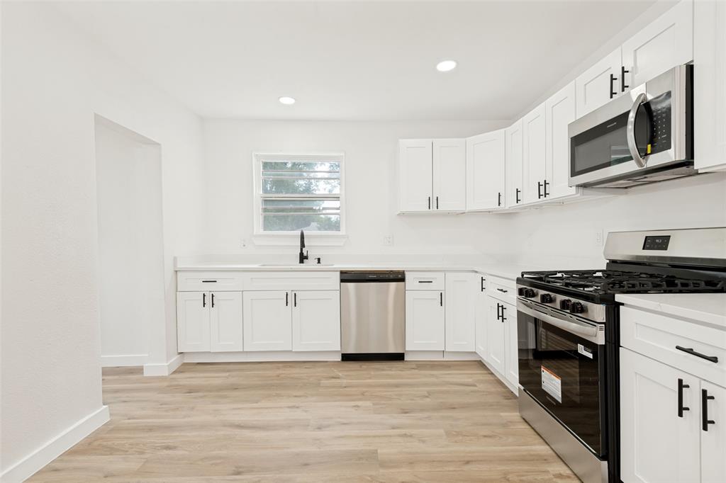 Modern kitchen featuring white shaker cabinetry with matte black hardware, light wood-finish flooring, stainless steel appliances, and a black faucet