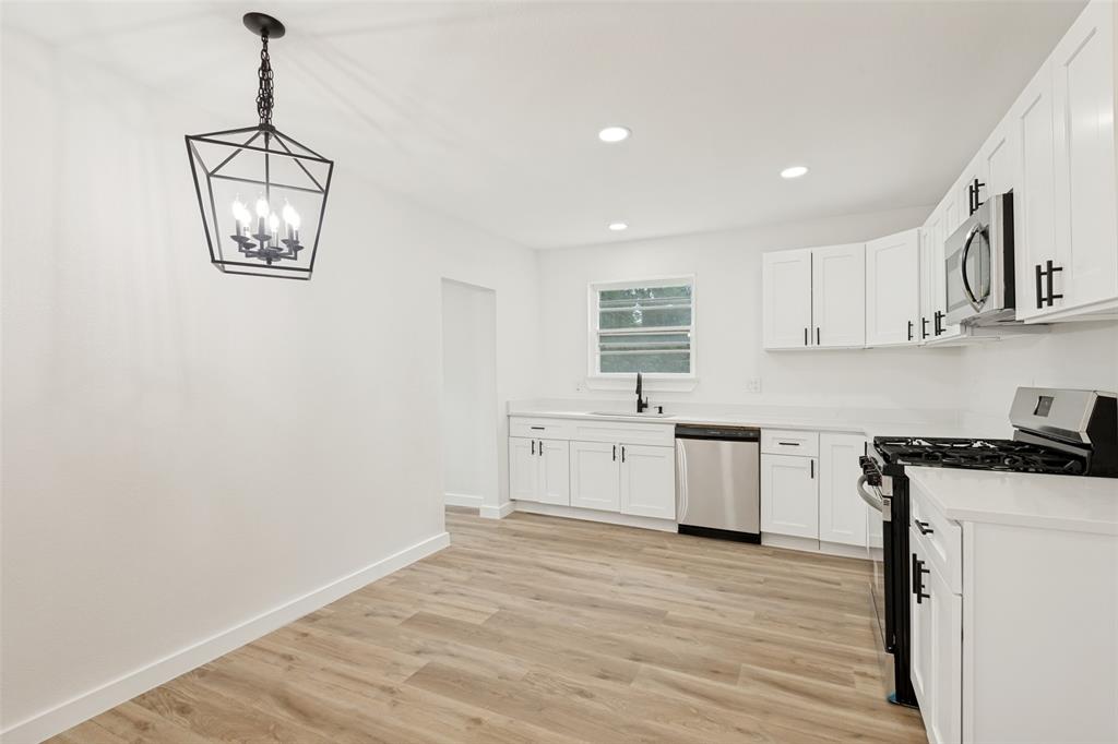 Modern kitchen featuring white shaker cabinetry, stainless steel appliances, light-toned wood-finish flooring, recessed lighting, and a contemporary black geometric chandelier