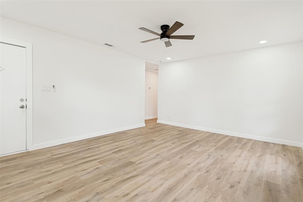 Spacious room featuring wood-finish flooring, crisp white walls, a ceiling fan with integrated lighting, and recessed ceiling lights