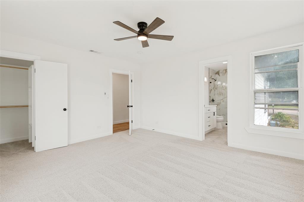 Carpeted room featuring a ceiling fan with light, an open closet with shelving, a window providing natural light, and an adjacent bathroom with a vanity and tiled shower