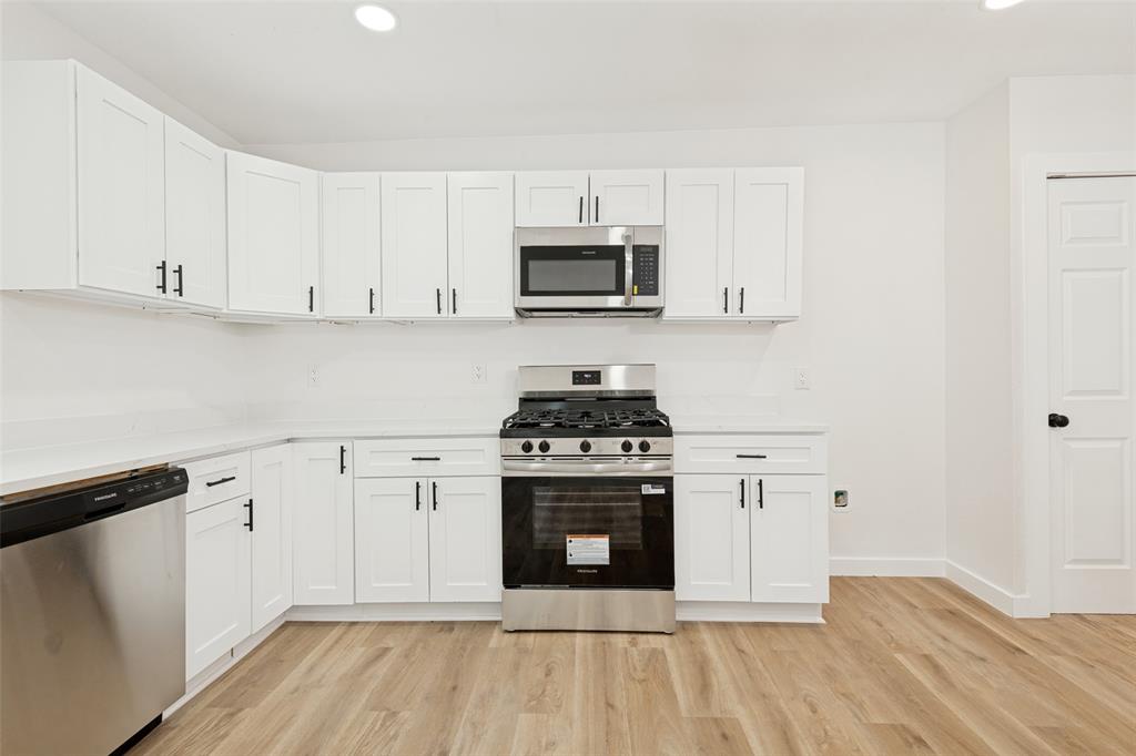 Modern kitchen featuring white shaker cabinetry, stainless steel appliances, light-toned countertops, wood-finish flooring, and recessed lighting