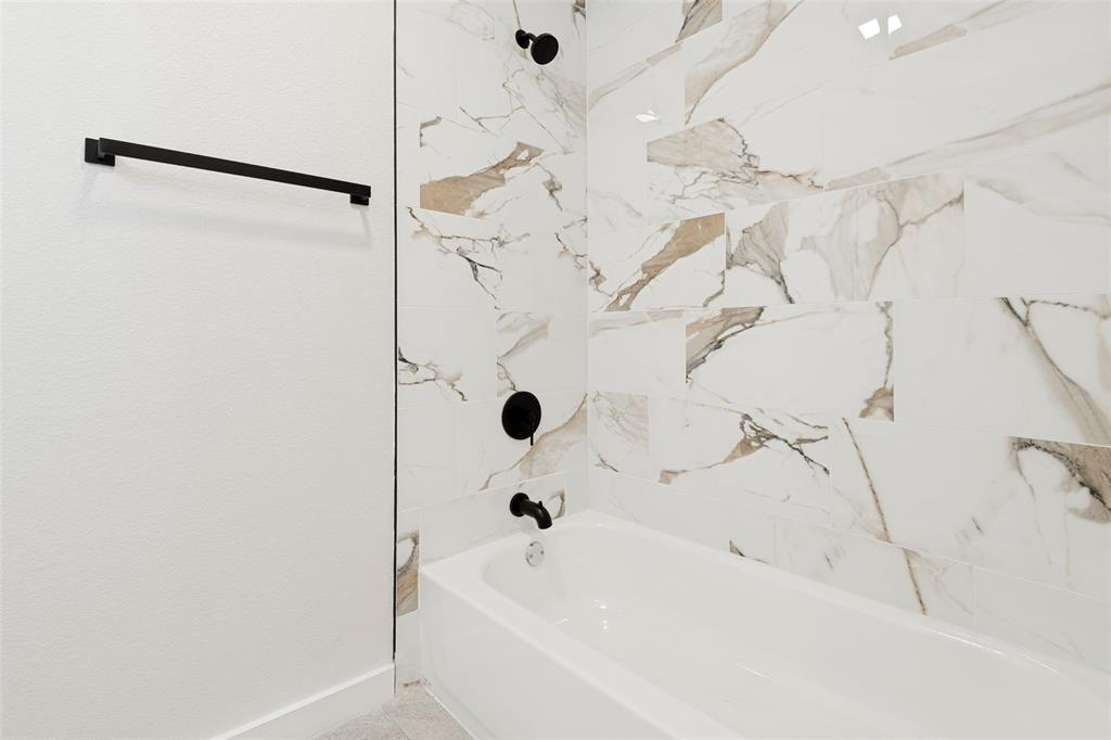 White bathtub with matte black fixtures, surrounded by large format porcelain wall tile featuring white, brown, and gray veining