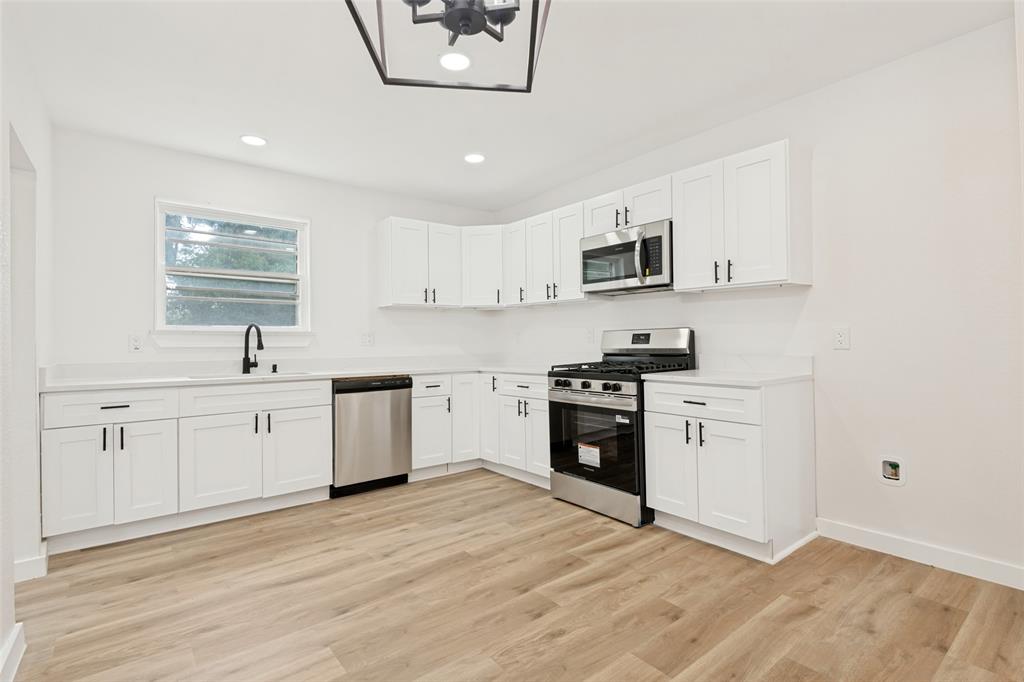 Contemporary kitchen featuring white cabinetry, light-toned countertops, stainless steel appliances, and wood-finish flooring