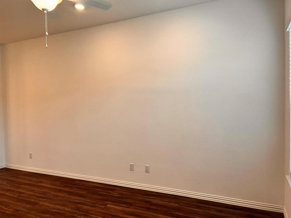 Spacious room featuring wood-finish flooring, white baseboards, and a ceiling fan with integrated lighting