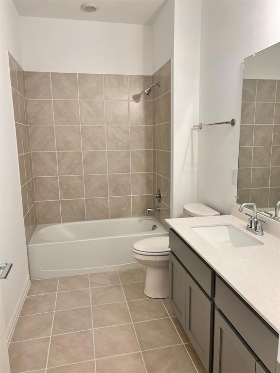 Bathroom featuring a full-size tub with tile surround, a built-in vanity with light-toned countertop and undermount sink, and tiled flooring