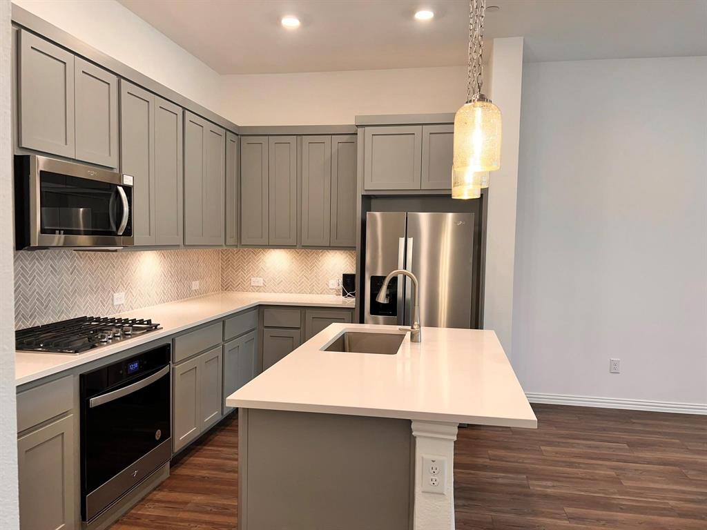Modern kitchen featuring sleek grey cabinetry, stainless steel appliances, a herringbone tile backsplash, and an island with an undermount sink