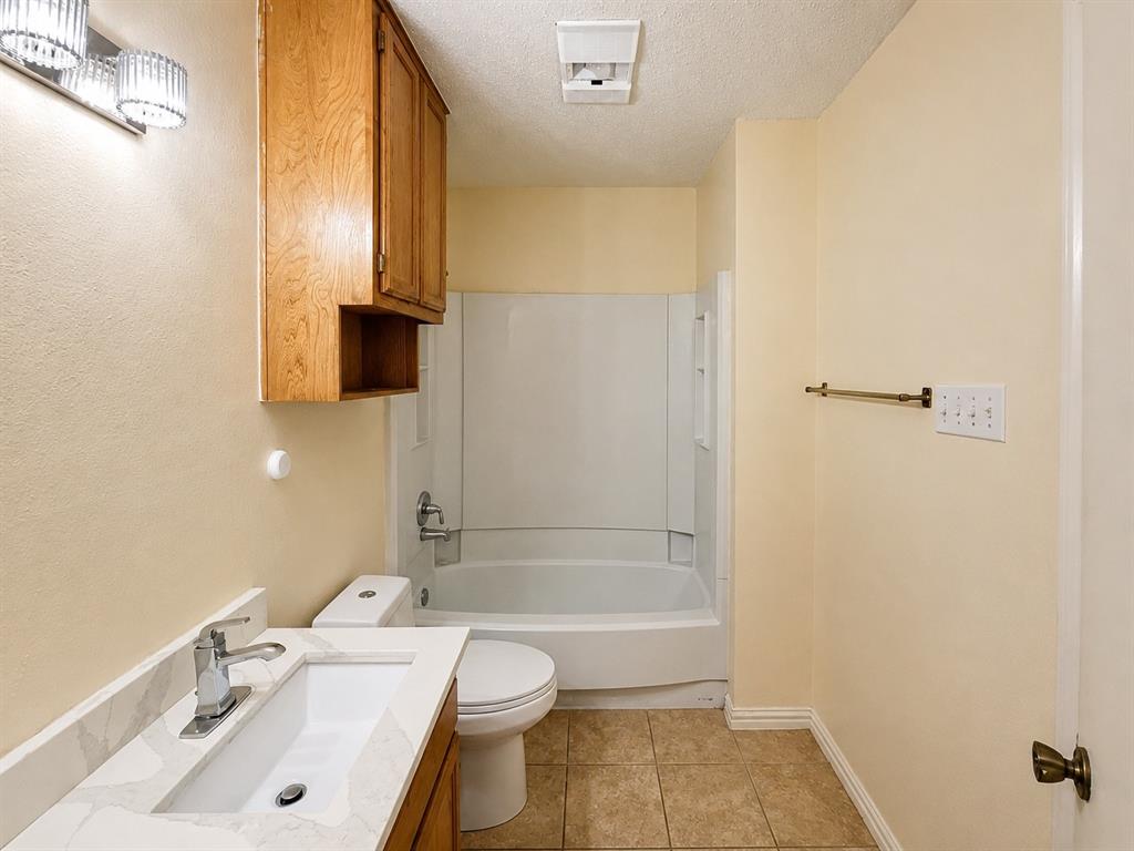 Bathroom featuring a white bathtub/shower combination, tile flooring, and a vanity with a white countertop and integrated sink Bathroom featuring a white bathtub/shower combination, tile flooring, and a vanity with a white countertop and integrated sink