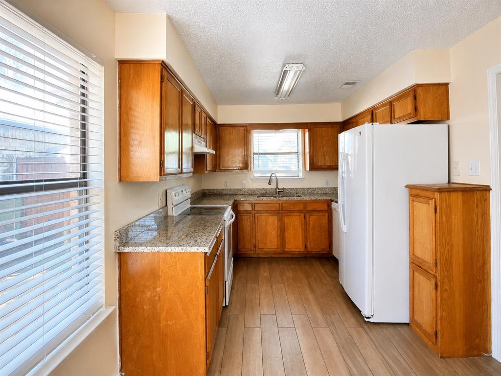 Kitchen featuring wood-finish flooring, wood cabinetry, granite countertops, and a stainless steel sink with a gooseneck faucet Kitchen featuring wood-finish flooring, wood cabinetry, granite countertops, and a stainless steel sink with a gooseneck faucet