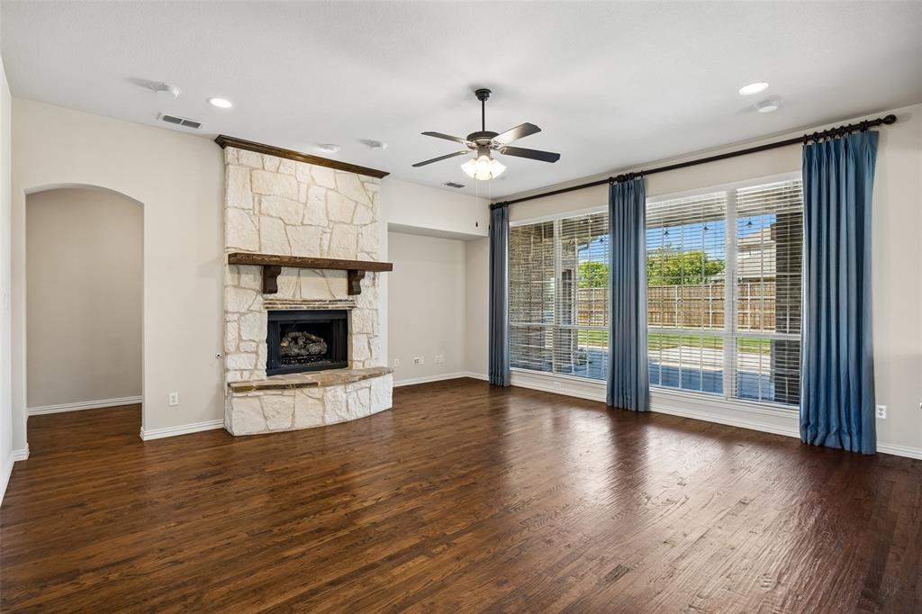 Spacious living area featuring wood-finish flooring, a stone fireplace with a wood mantle, and multiple large windows