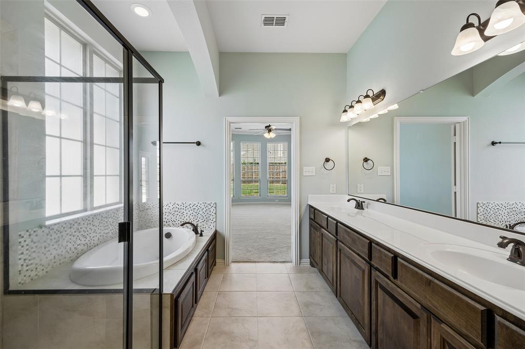 Bathroom featuring a built-in soaking tub with mosaic tile surround, a spacious double vanity with integrated sinks, and an enclosed shower with clear glass panels