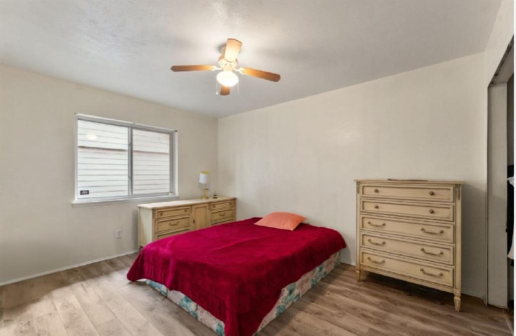 Wood-finish flooring, ceiling fan with integrated lighting, and a single window with horizontal blinds