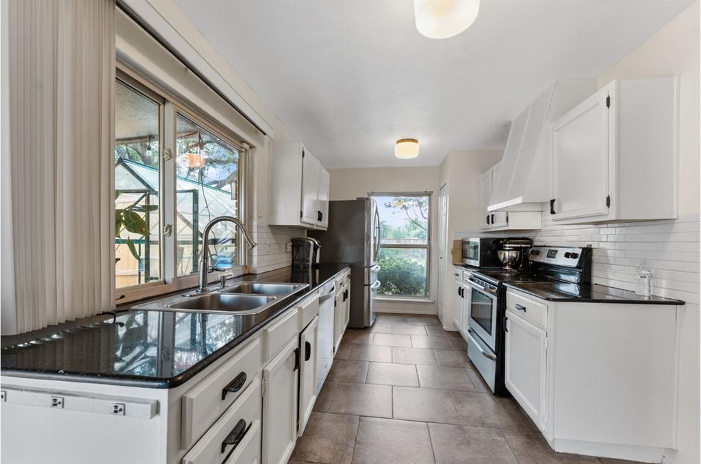 Kitchen featuring white cabinetry, black countertops, tile flooring, and a stainless steel double basin sink